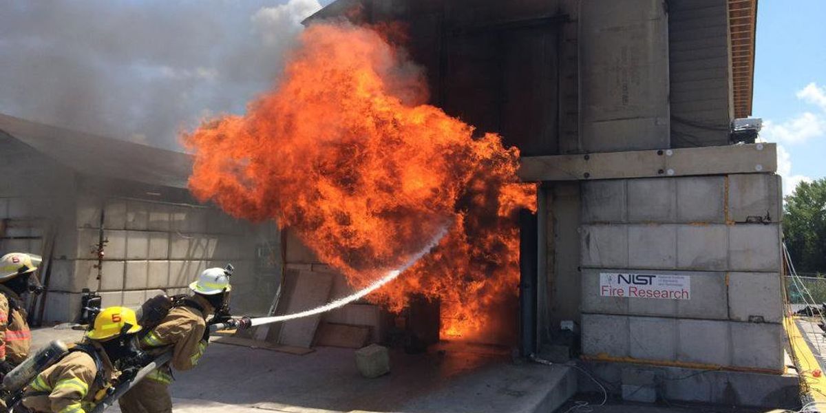 NIST firefighters douse flames bursting from a building as a flashover occurs during an experiment.  Credit: NIST