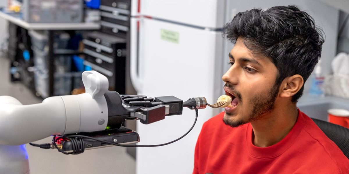Doctoral student Rajat Kumar Jenamani, a member of Tapomayukh Bhattacharjee’s EmPRISE Lab, prepares to take a piece of a banana from an assistive robot prototype. Ryan Young/Cornell University
