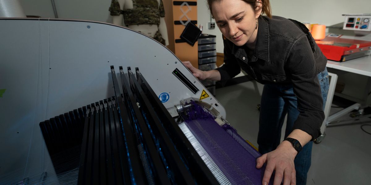 At Lincoln Laboratory’s Defense Fabric Discovery Center, Erin Doran demonstrates how reflective fibers can be woven into textiles. Such fibers could function as indelible, scannable labels to easily sort fabrics for recycling. Photo: Glen Cooper