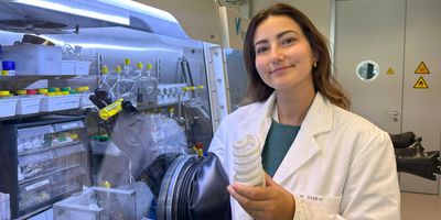 ETH doctoral student Marie Perrin presents the new recycling approach. In her left hand, she is holding the raw material in the form of a fluorescent lamp and, in her right, the yellow reagent that can separate rare earth metals. (Photograph: Fabio Masero / ETH Zurich)