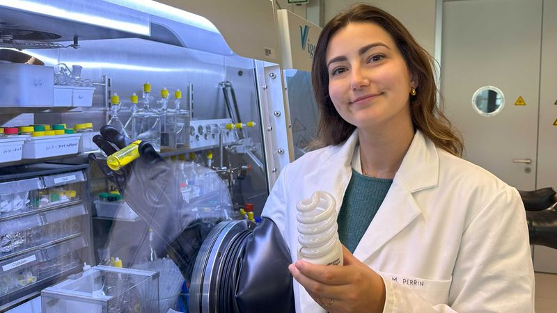 ETH doctoral student Marie Perrin presents the new recycling approach. In her left hand, she is holding the raw material in the form of a fluorescent lamp and, in her right, the yellow reagent that can separate rare earth metals. (Photograph: Fabio Masero / ETH Zurich)