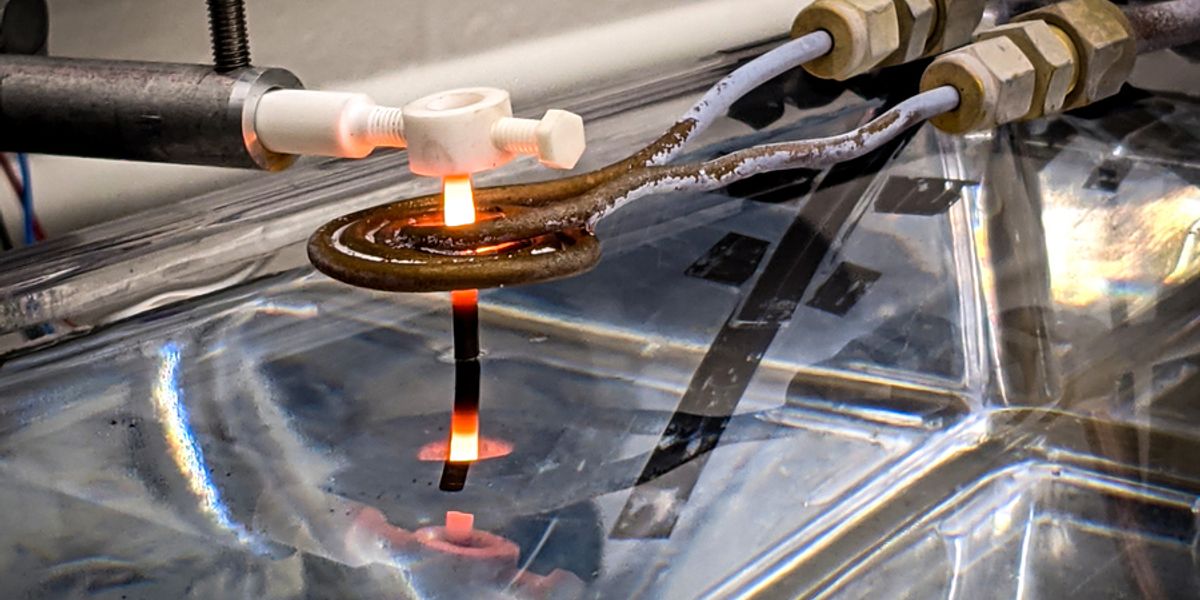 A thin rod of 3D-printed superalloy is drawn out of a water bath, and through an induction coil, where it is heated to temperatures that transform its microstructure, making the material more resilient. The new MIT heat treatment could be used to reinforce 3D-printed gas turbine blades. Credit: Dominic David Peachey