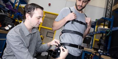 Researcher Aaron Young makes adjustments to an experimental exoskeleton worn by then-Ph.D. student Dean Molinaro. The team used the exoskeleton to develop a unified control framework for robotic assistance devices that would allow users to put on an "exo" and go — no extensive training, tuning, or calibration required. (Photo: Candler Hobbs)