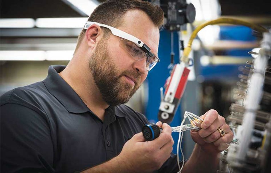 White bearded man wearing google glass examining a cluster of wires. 