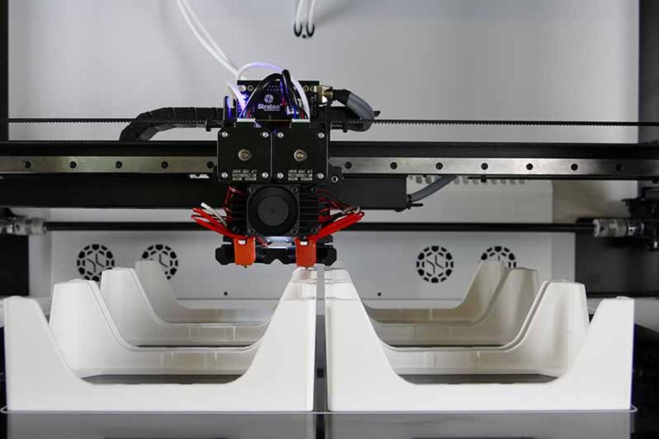 A 3D printer printing white plastic shapes.