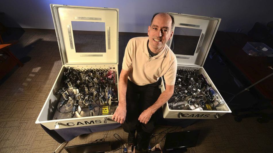 A picture of CAMS cofounder Peter Jenniskens, seen between two CAMS base station boxes with their lids lifted to show the camera system contained inside.