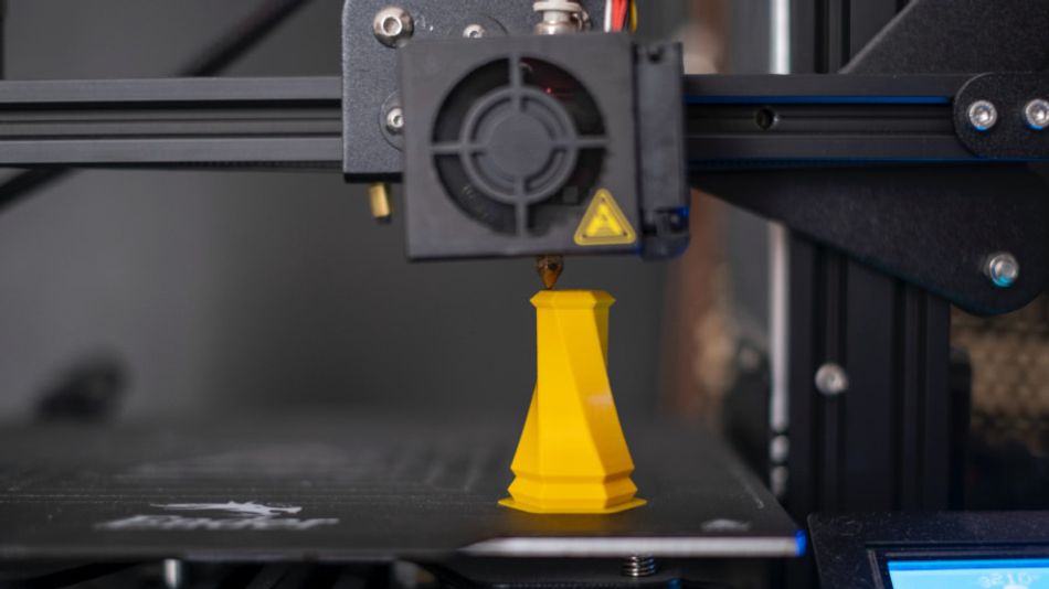 A picture of a 3D printer extruding a tall, twisted vase-shaped object.
