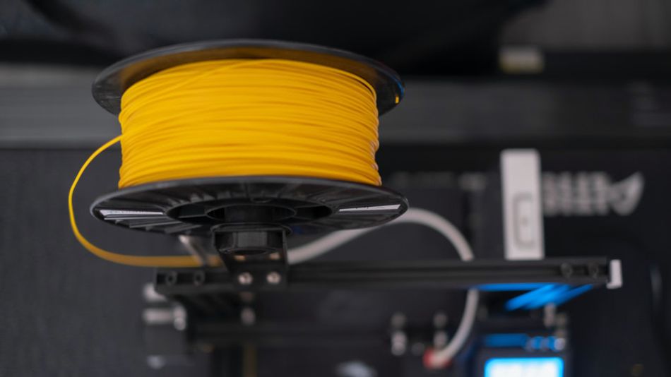 A photo of a spool of 3D print filament, being fed into an extruder.