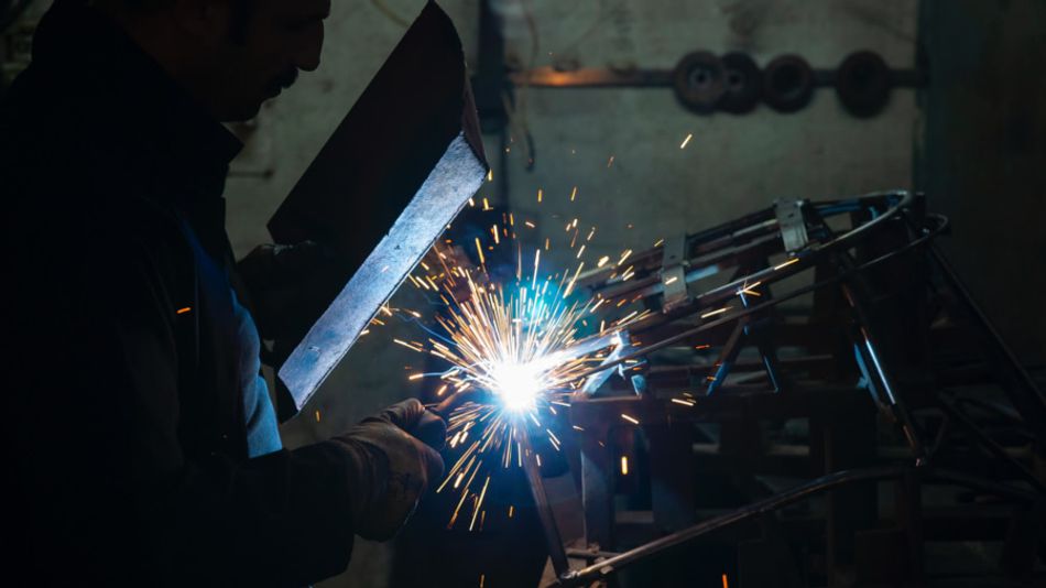 A photograph of a welder holding a mask between their eyes and the piece being welded; sparks can be seen flying on the other side of the mask.