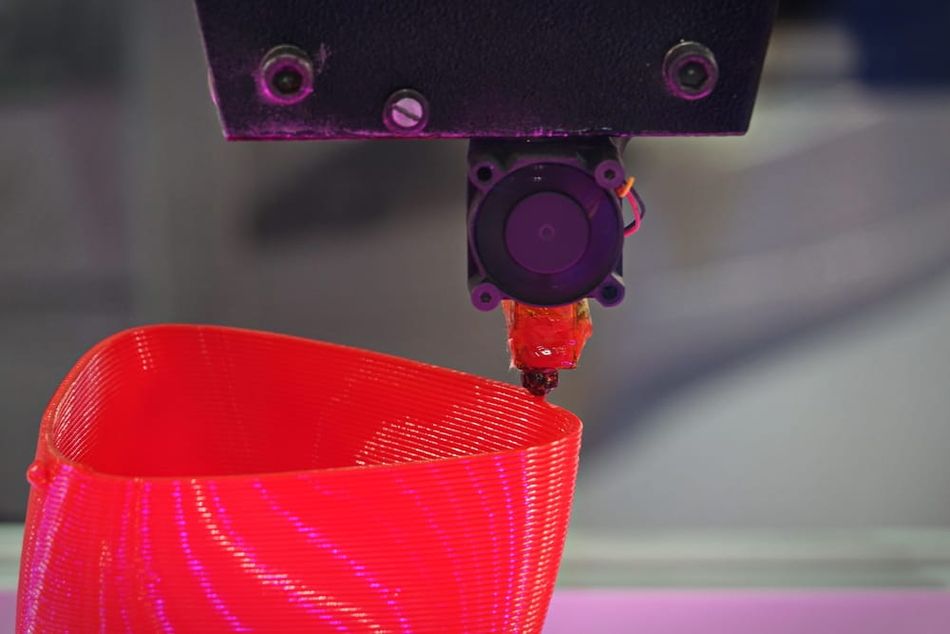 3D printer nozzle extruding red filament