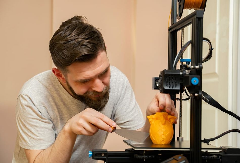 Man removes 3D print using putty knife