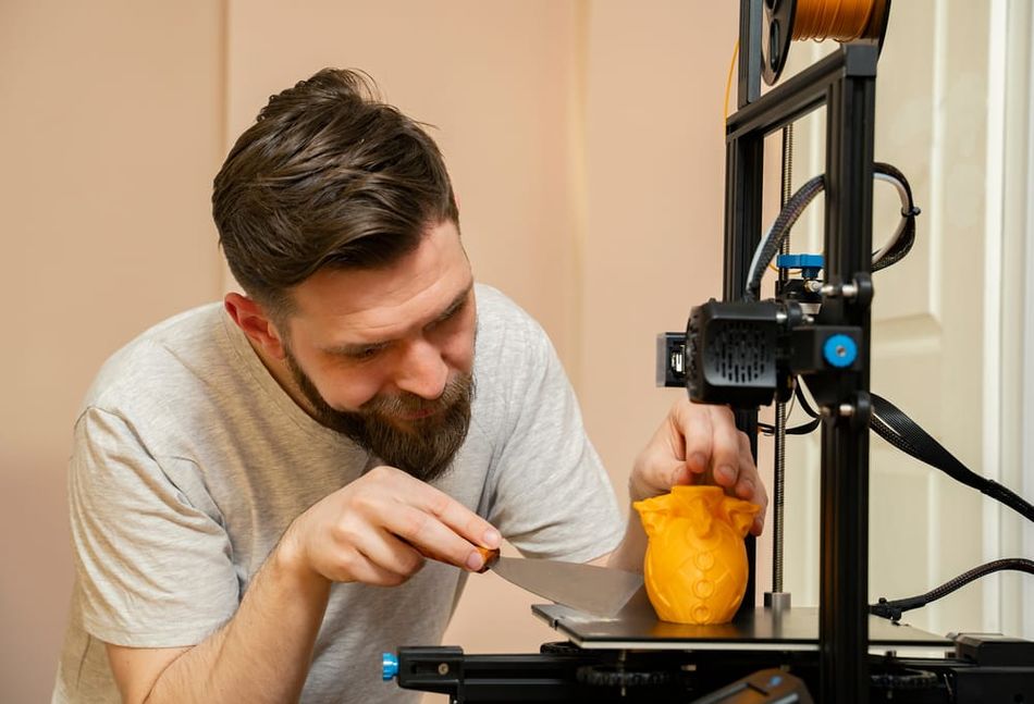 Man removes 3D print using putty knife