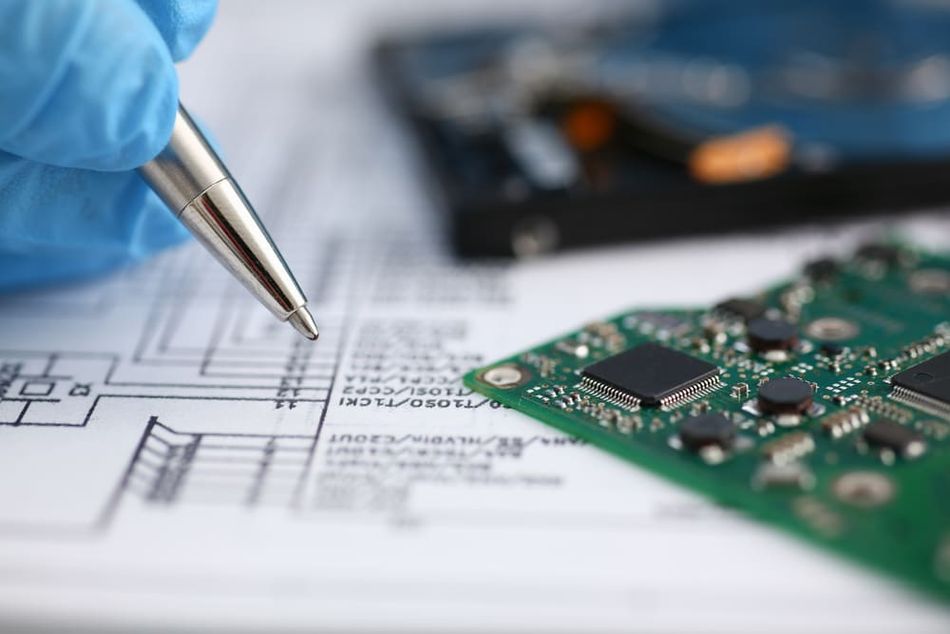 Electronic product design idea with a PCB in front of a schematic capture, a basic two-dimensional circuit diagram displaying the connectivity and functionality of various electrical components.