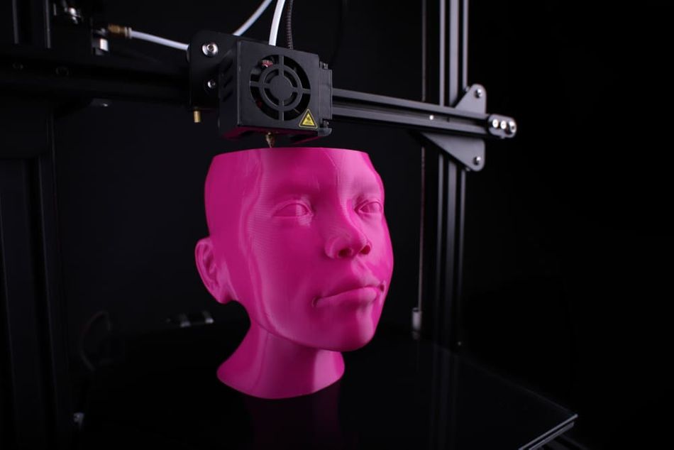 A cartesian 3D-printer makes a humanoid head from pink plastic