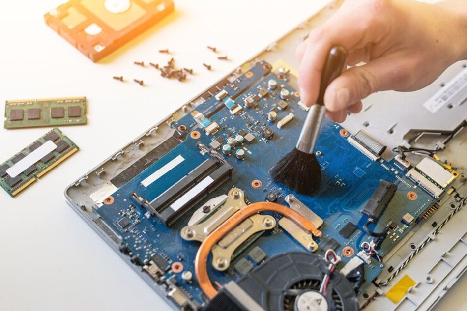 Technician cleaning circuit board of disassembled laptop.