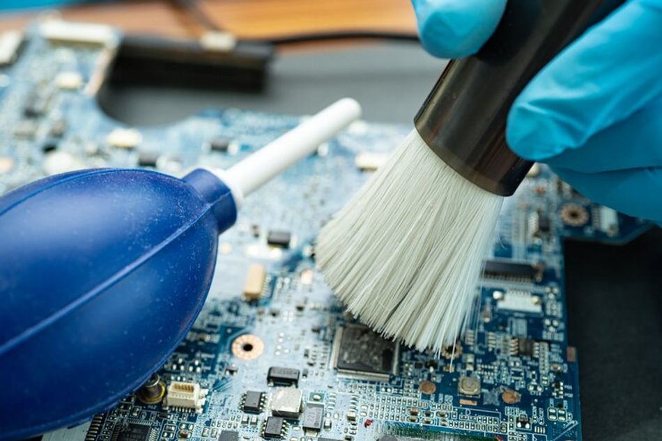 Technician using a bristle brush and air blower ball to clean dust in circuit board computer.