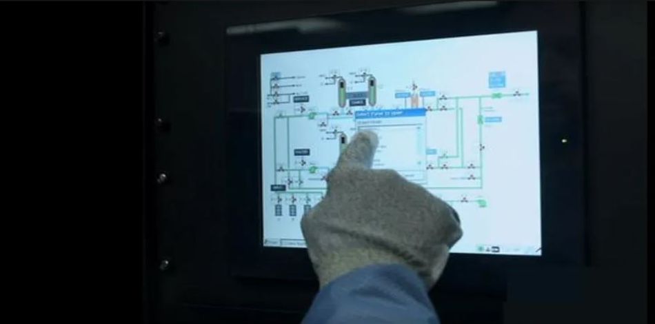 An engineer working in industrial setting, using HMI of SCADA system to control production process.