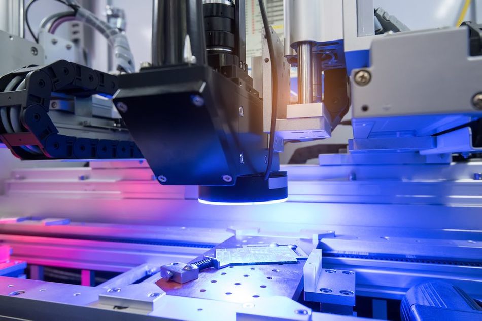 A close-up of a robotic arm carrying a machine vision system while working on a manufacturing line illuminated by purple and blue lighting.