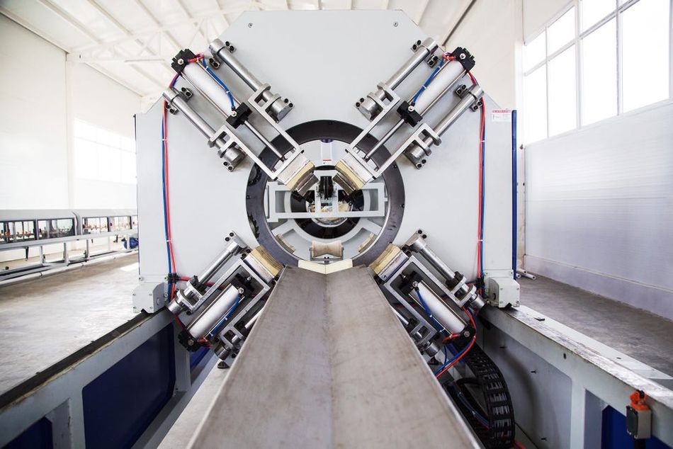 A close-up view of a high-tech industrial machine used for the production of polyurethane foam pipes in a factory. The image showcases the complex assembly of the HDPE pipe manufacturing equipment, featuring multiple hydraulic arms, metal components, and electrical wiring.