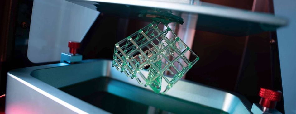 A green lattice structure being printed by a 3D printer with a dark background.