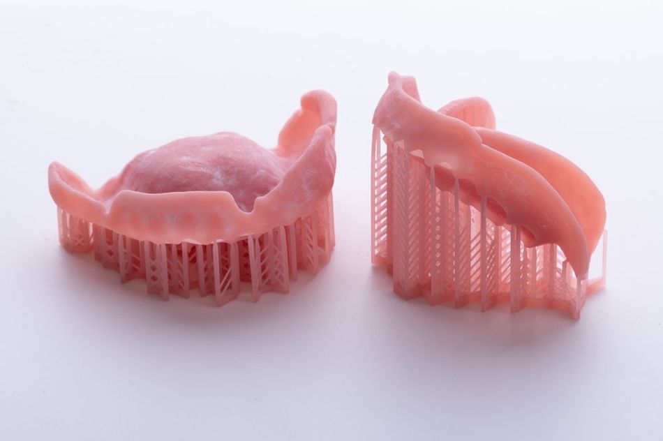 Two pink dentures base with support structures on a white background.