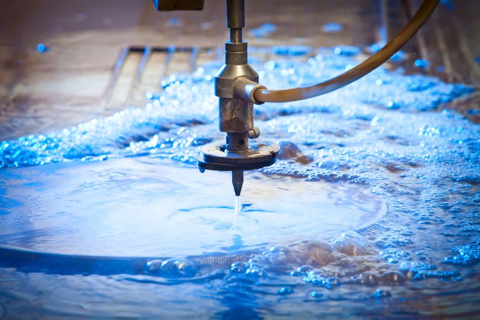 Close-up view of a water jet cutting machine at work, precisely slicing through a steel plate. The image captures the intense precision of the cutting process, with water and metal fragments dispersed during the operation.