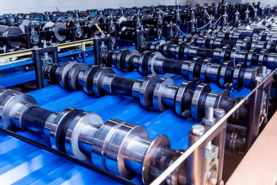 A metal sheet forming machine at a modern metalwork factory, showcasing a series of rollers used for shaping blue coloured metal sheets into specific profiles.