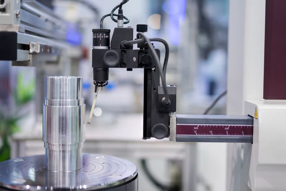 A contour measuring machine inspecting the roughness of a cylindrical metal part in a workshop. The machine's probe is positioned to assess the surface finish and precision of the component