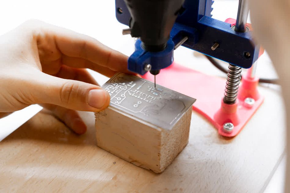 An engineer manually drilling holes in a PCB for a DIY project