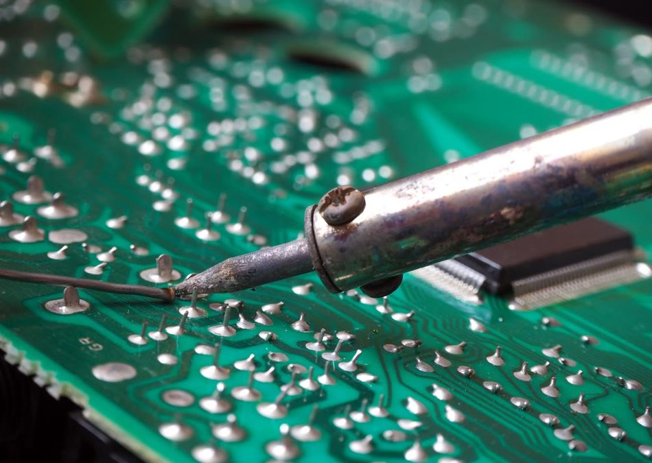 Close-up of a soldering iron applying solder to electronic components on a green printed circuit board (PCB)