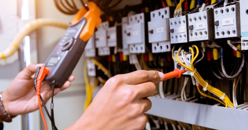A technician using a DMM to test relay output in a control panel