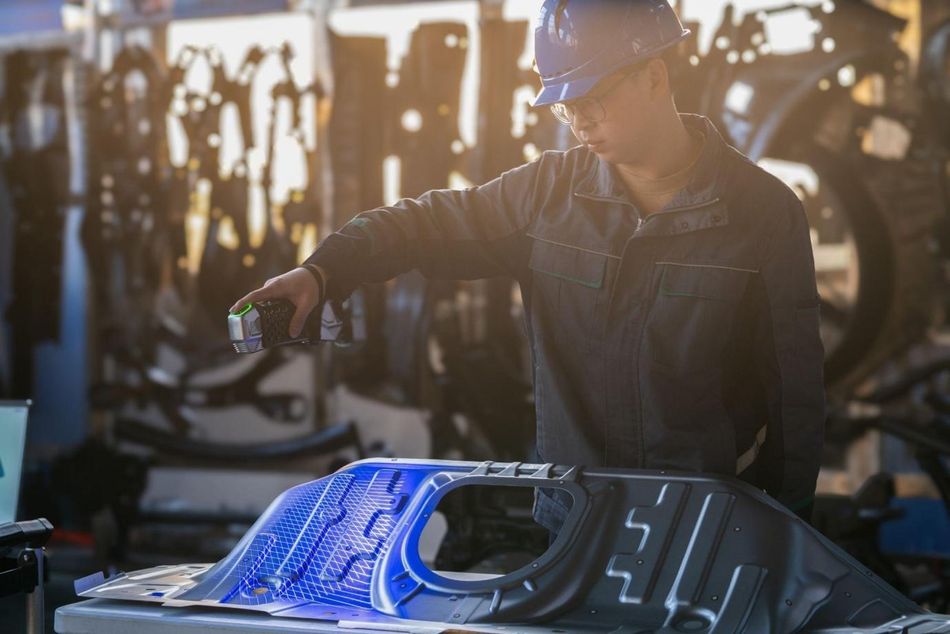 An operator uses a handheld 3D scanner to capture the surface geometry of an automotive panel