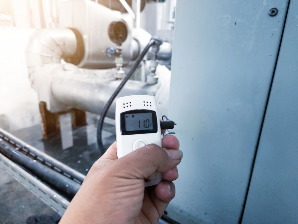 Handheld digital temperature meter measuring the surface temperature of industrial piping and equipment in a processing facility. The image illustrates practical temperature monitoring used to evaluate thermal gradients, a critical requirement for studying the Seebeck effect, thermoelectric performance, and industrial heat recovery applications.