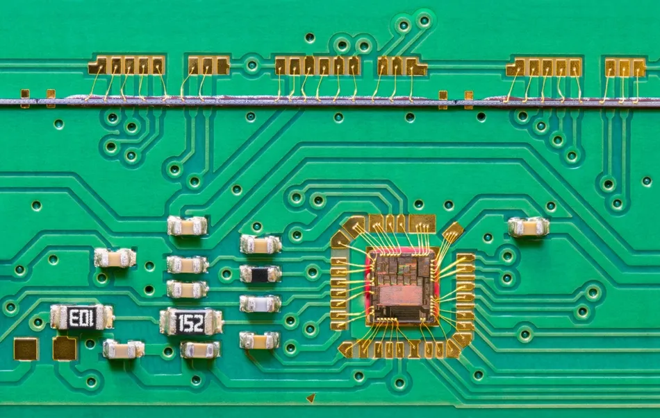 This image shows a close-up of a printed circuit board (PCB) with an integrated circuit (IC) die connected via fine gold bonding wires.