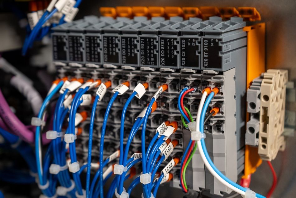 Close-up view of an electrical control panel containing multiple DIN-rail-mounted components, terminal blocks, wiring, and control devices arranged within an industrial cabinet.